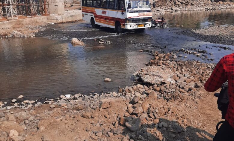 पानी और पत्थरों के बीच से निकलती बस और दुपहिया वाहन, भीमगढ़ नदी पर अधूरे पुल के कारण जोखिमभरा मार्ग।