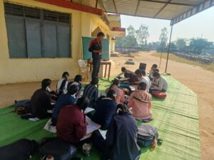 धारनाकला विद्यालय में छात्र बरामदे में दरी बिछाकर पढ़ाई करते हुए